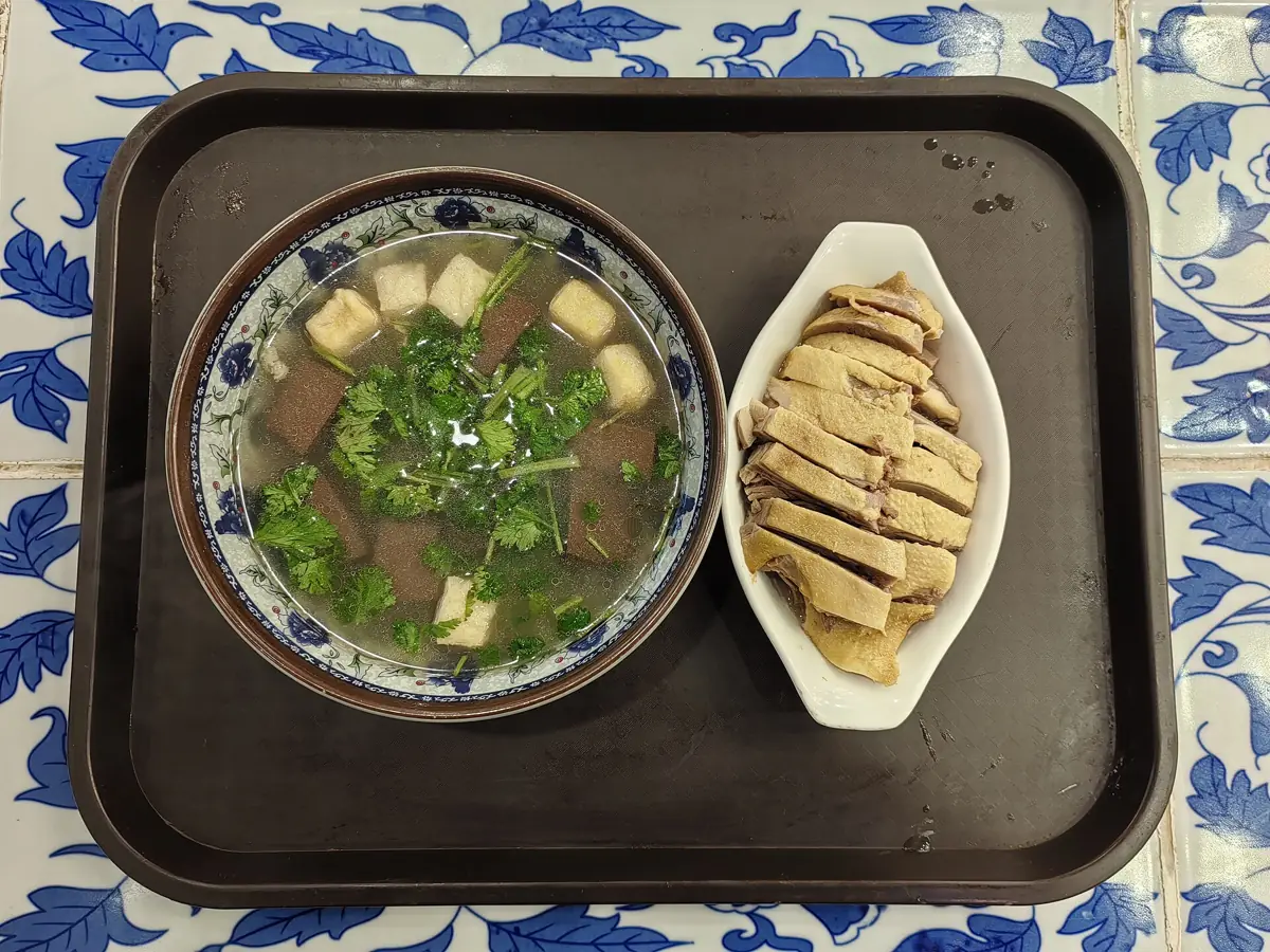 A bowl of duck blood and vermicelli soup beside a plate of salted duck