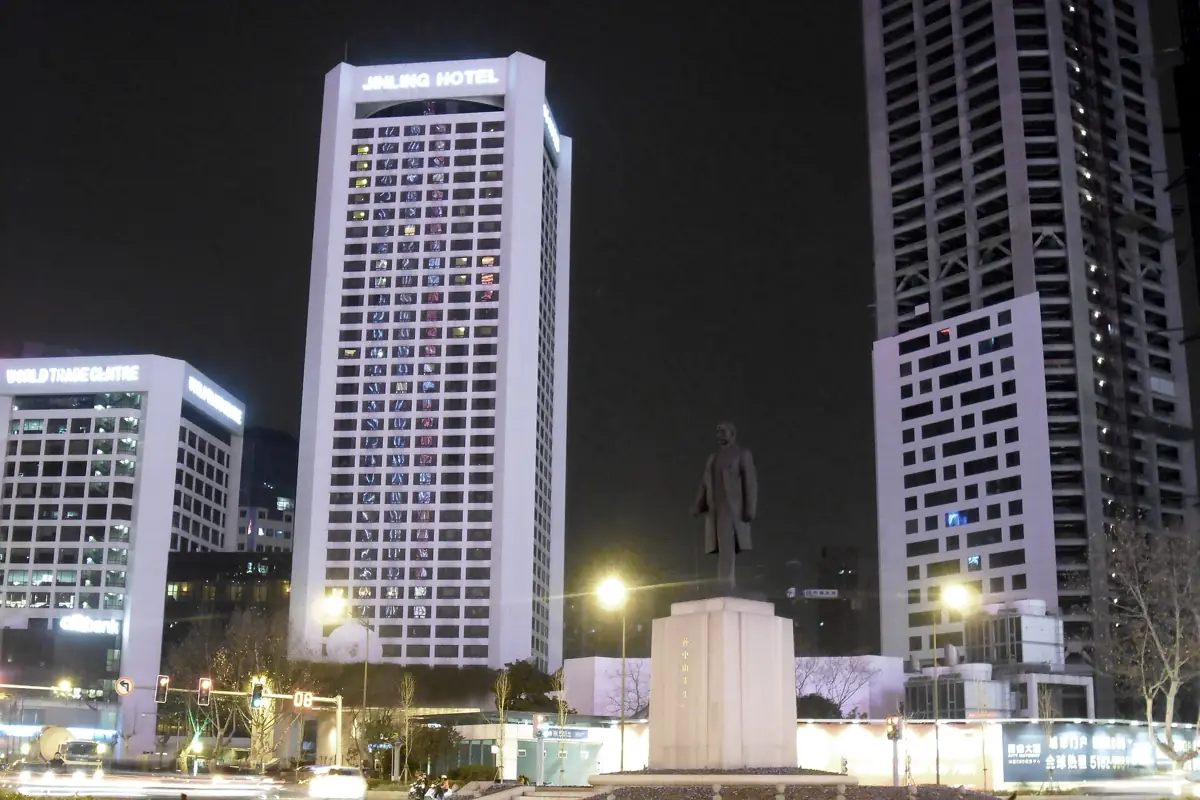 Night view of Xinjiekou Square with the Sun Yat-sen statue and the tall white tower of the Jinling Hotel behind